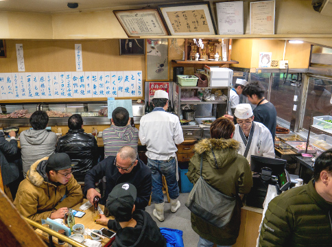 The interior of Toritake, customers seated at closely packed tables with staff in white working between them